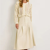 Cream vegan leather midi skirt with box pleats and fixed waistband, styled with ivory knit sweater