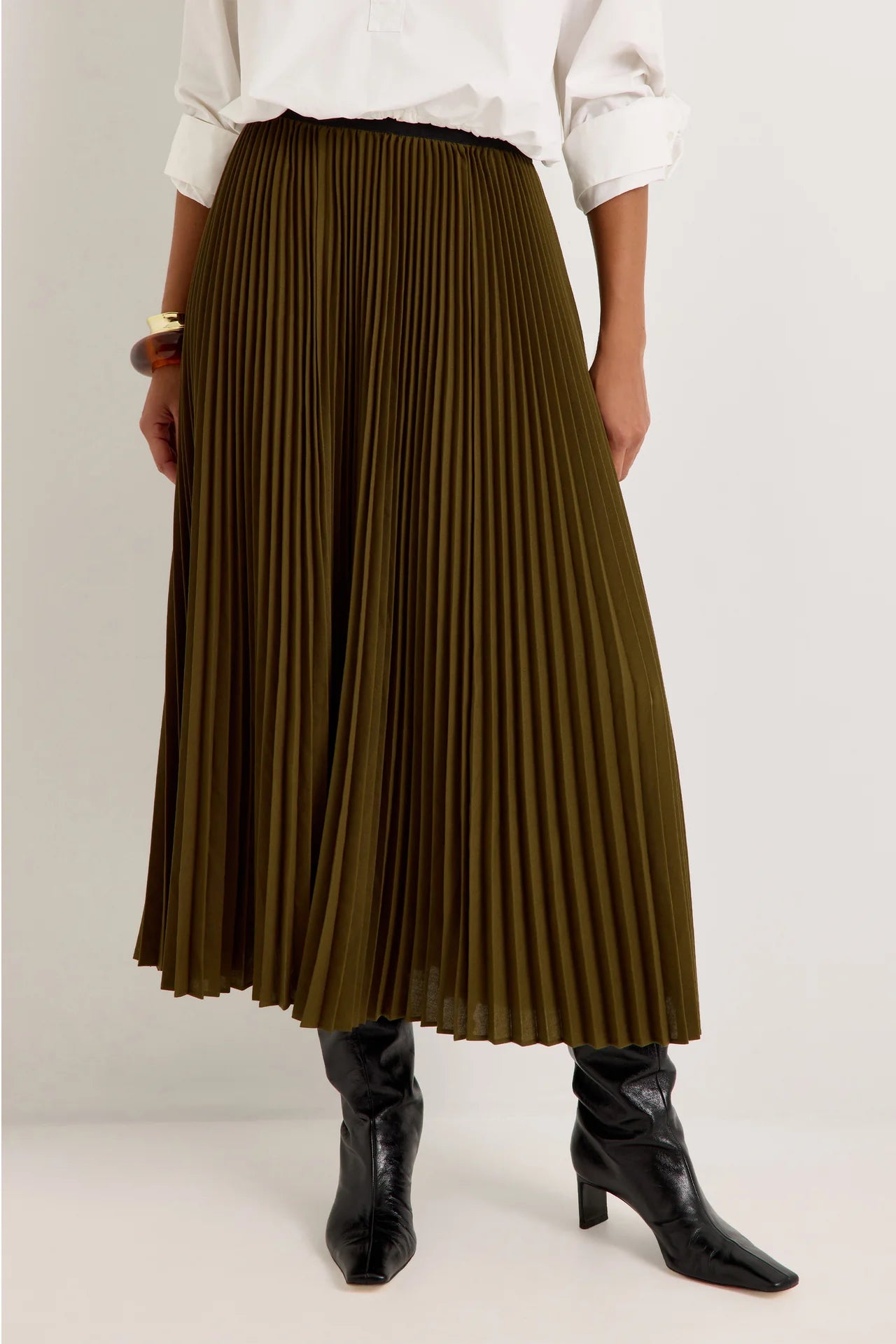 Olive green pleated midi skirt with black elastic waistband, styled with black knee-high boots