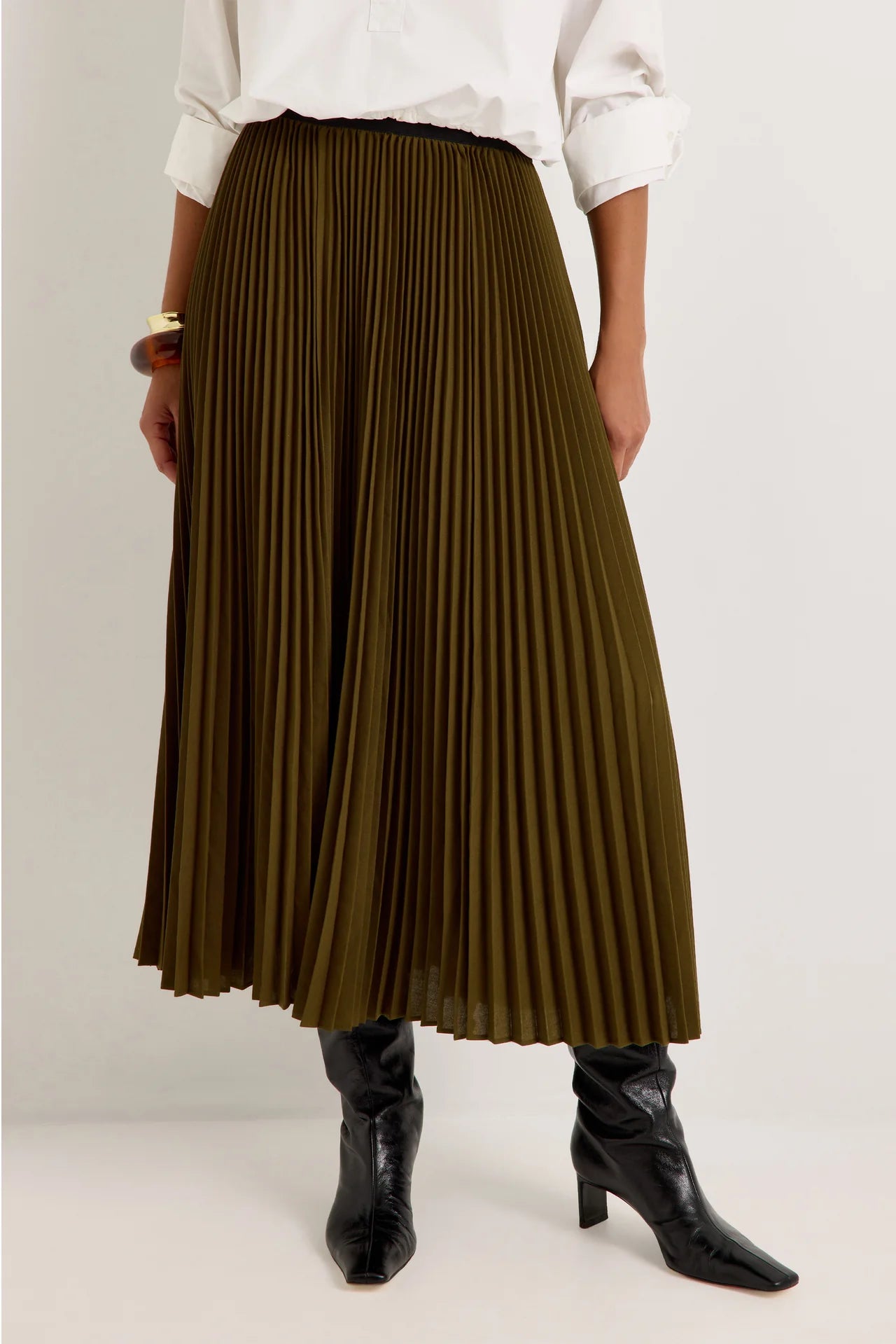 Olive green pleated midi skirt with black elastic waistband, styled with black knee-high boots
