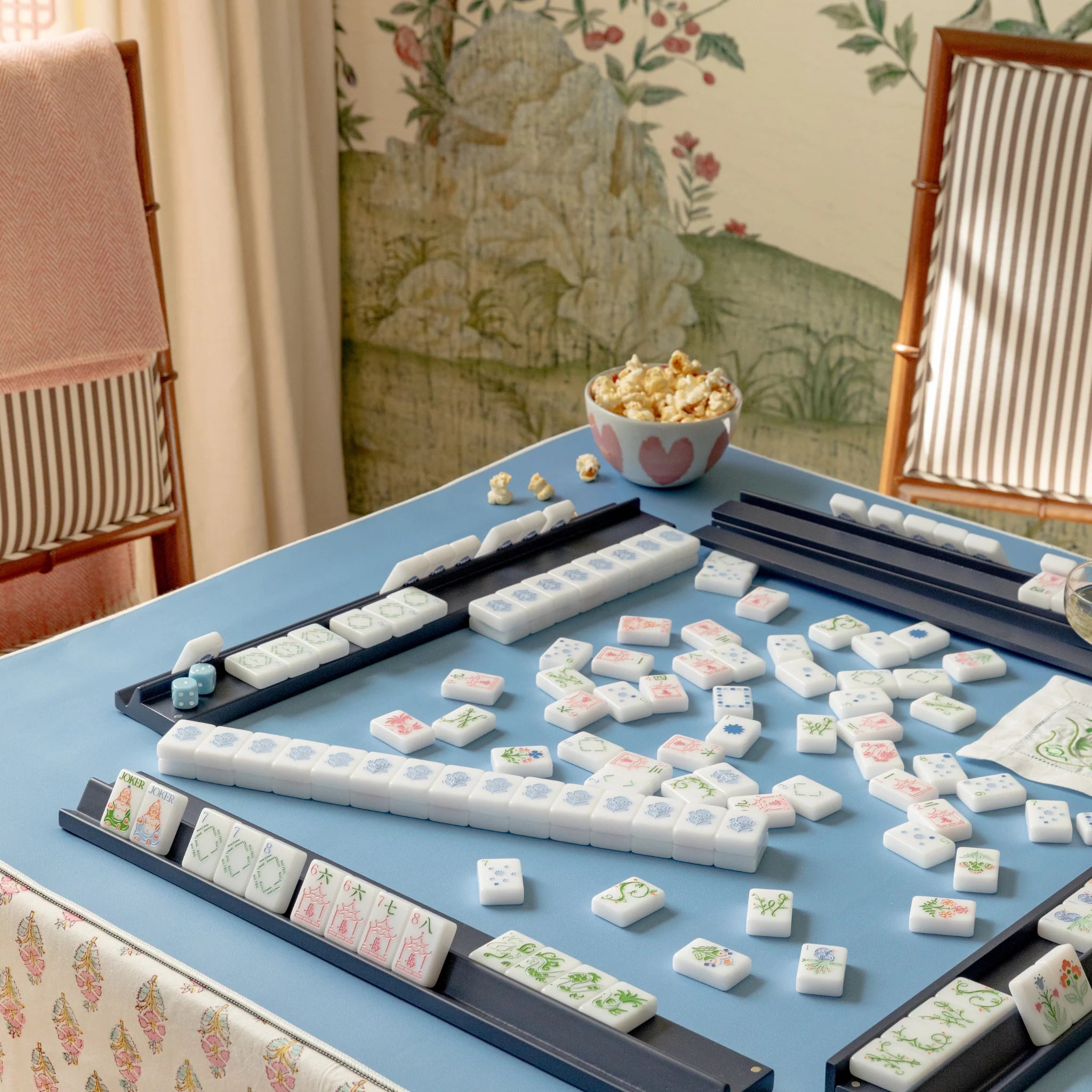 Navy high-gloss wooden mahjong racks with white floral tiles on blue game table