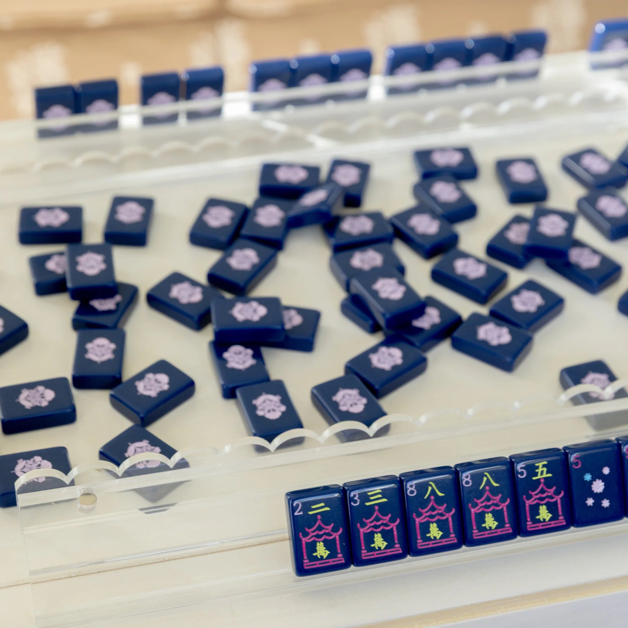 Clear scalloped acrylic mahjong racks with navy blue tiles on a white surface