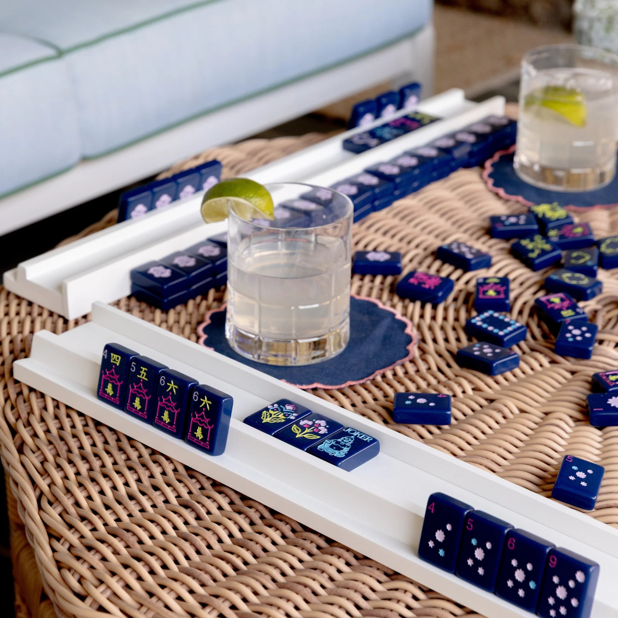 White high-gloss wood mahjong racks holding navy blue decorative tiles on wicker table