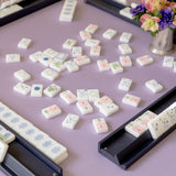 White mahjong tiles with pastel floral designs scattered on a lavender neoprene game mat