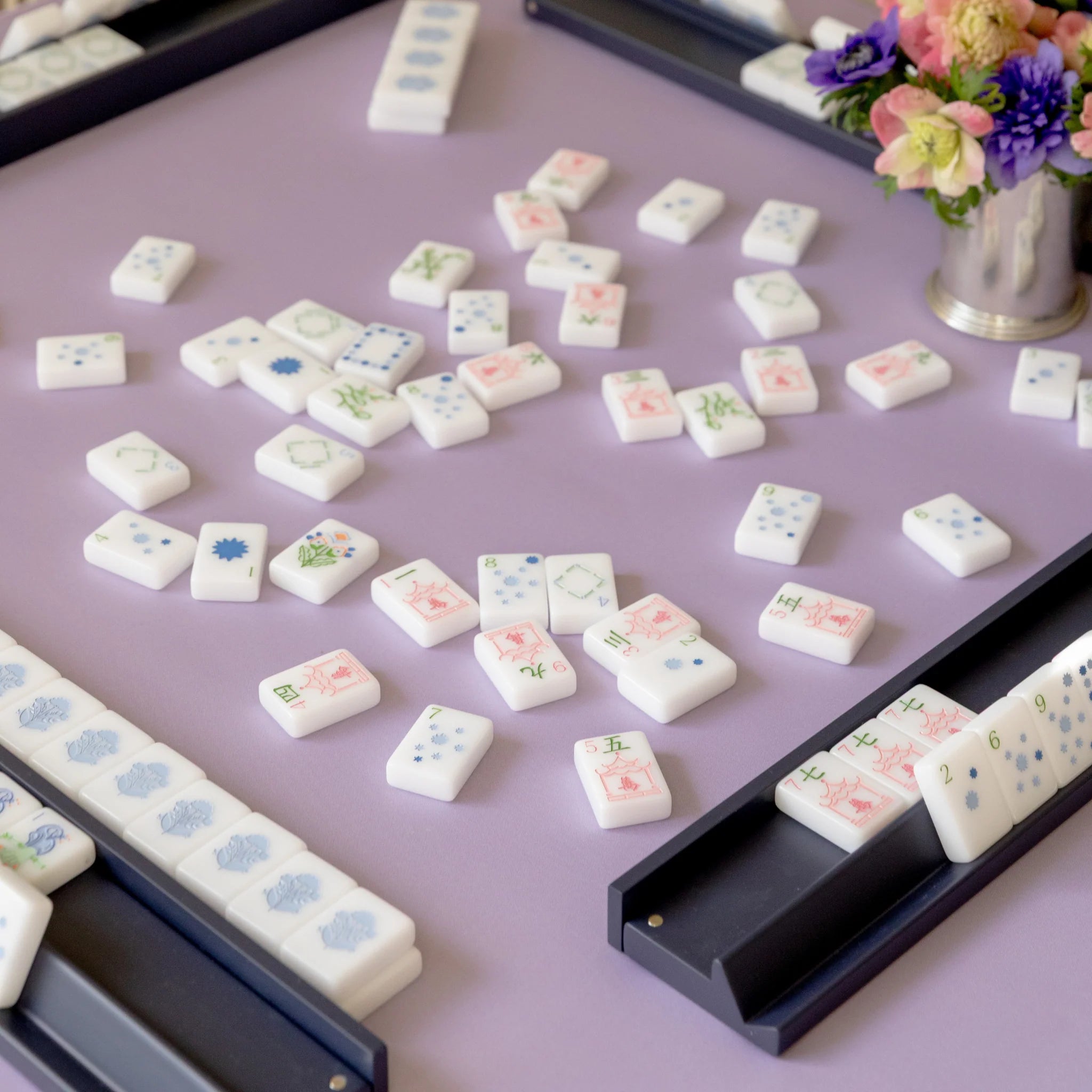 White mahjong tiles with pastel floral designs scattered on a lavender neoprene game mat