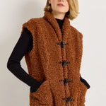 Brown sherpa fleece vest with black toggle closures worn over black ribbed knit