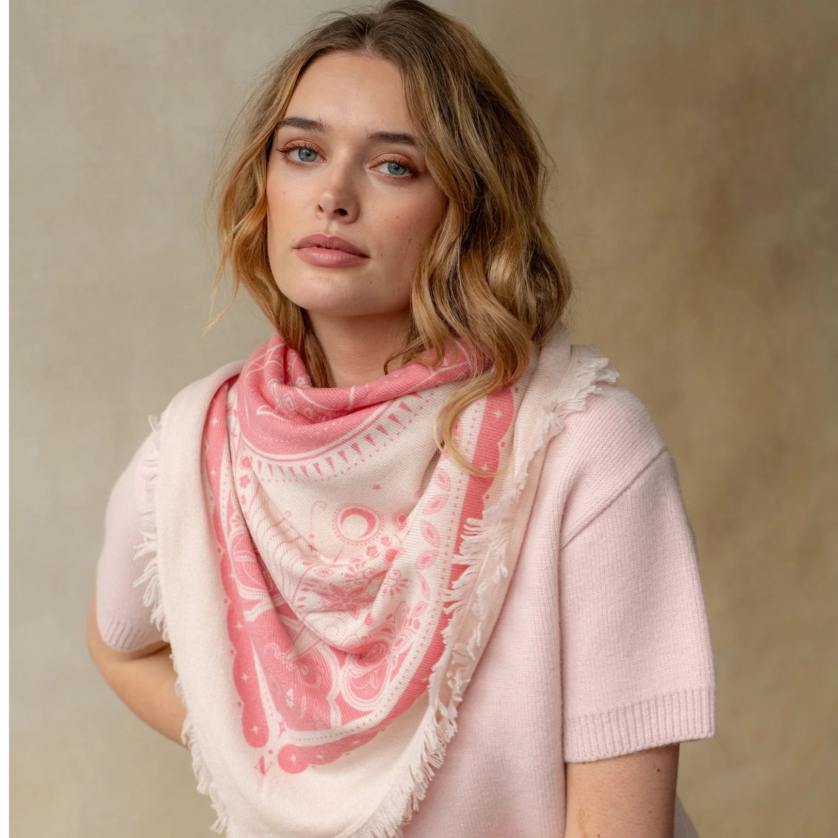 Pink and white celestial print cashmere bandana wrap with fringe trim, styled loosely around neck