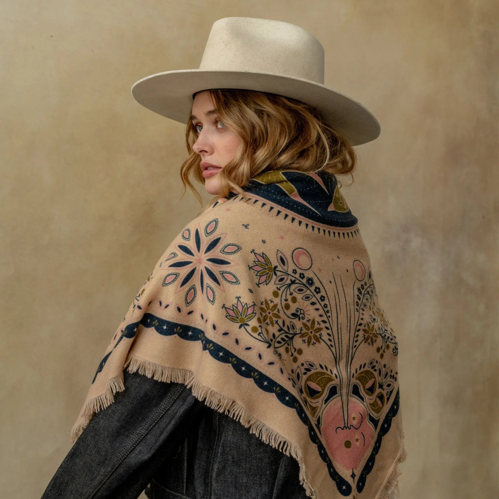 Beige celestial floral patterned cashmere wrap with fringe, styled over dark jacket